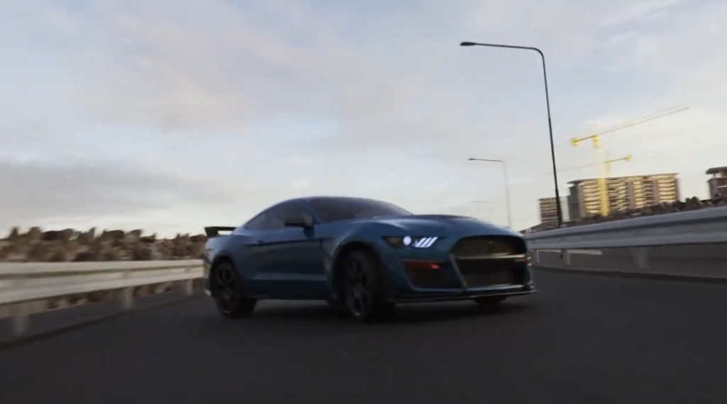 Blue Ford Mustang Shelby GT500 driving on a multi-lane highway at dusk, with street lights and buildings visible in the background