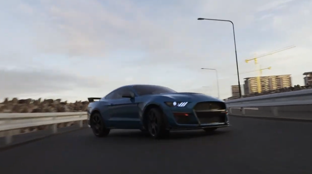 Blue Ford Mustang Shelby GT500 driving on a multi-lane highway at dusk, with street lights and buildings visible in the background