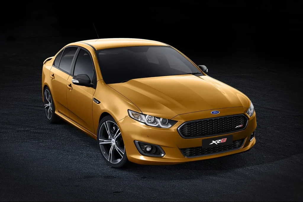 Golden-yellow Ford FGX Falcon XR8 sedan shown from three-quarter front angle against dark background, featuring aggressive front grille, LED headlights, and alloy wheels
