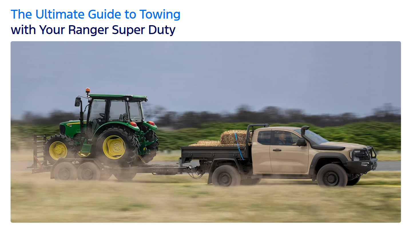 Tan Ford Ranger Super Duty towing a green John Deere tractor with hay bales on a dirt road, motion blur effect