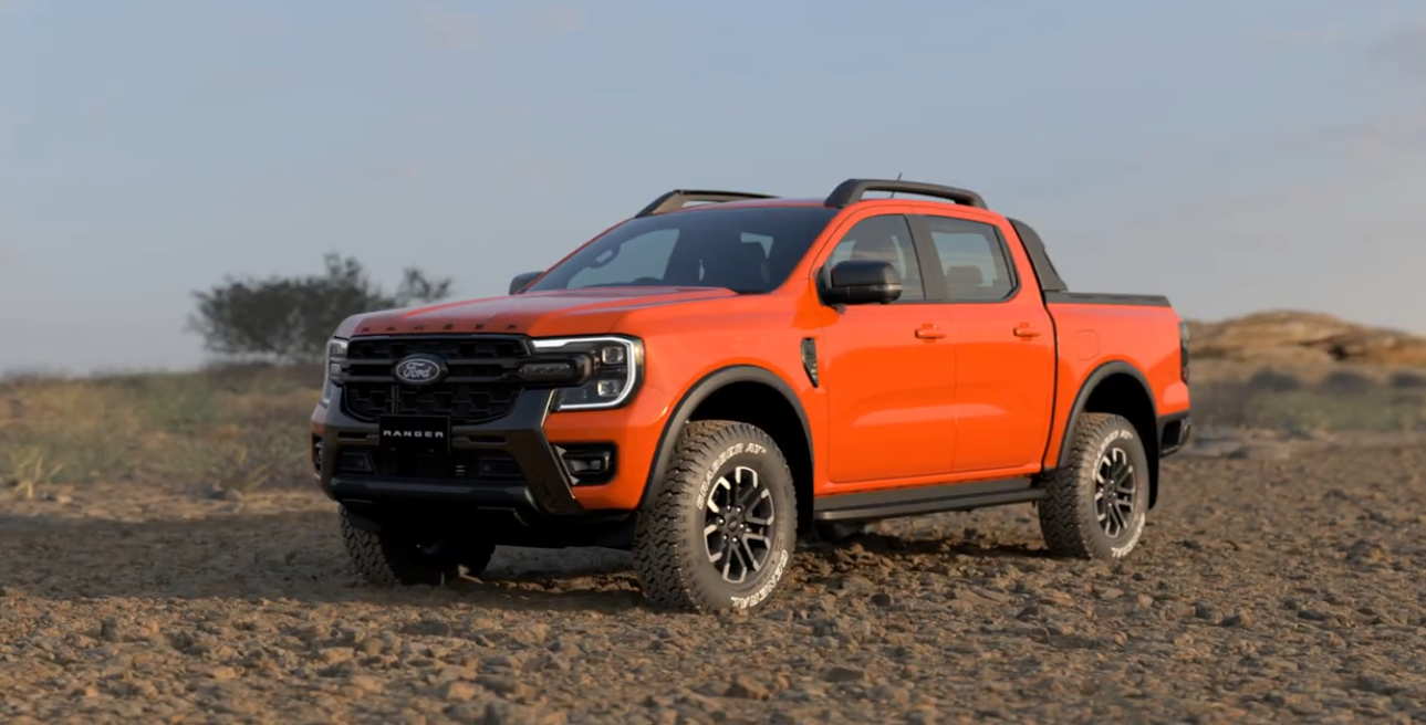 Orange Ford Ranger pickup truck parked on arid, rocky terrain with sparse vegetation and hills in the background