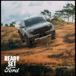 White Ford Ranger Raptor pickup truck on off-road terrain with dry grass and trees in background under cloudy sky
