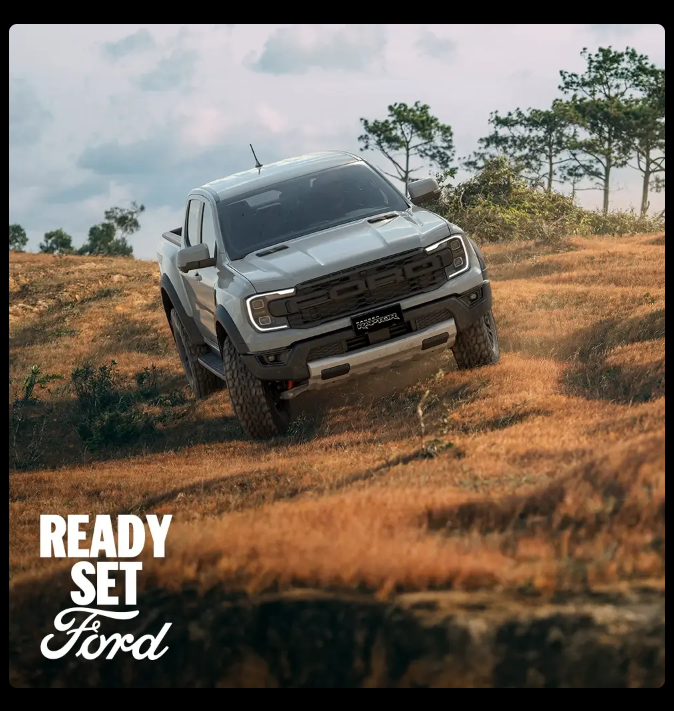 White Ford Ranger Raptor pickup truck on off-road terrain with dry grass and trees in background under cloudy sky