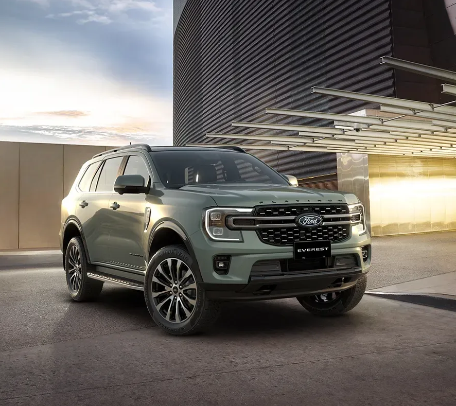 Ford Everest SUV in light green parked in modern architectural setting with corrugated metal building and glass canopy at dusk