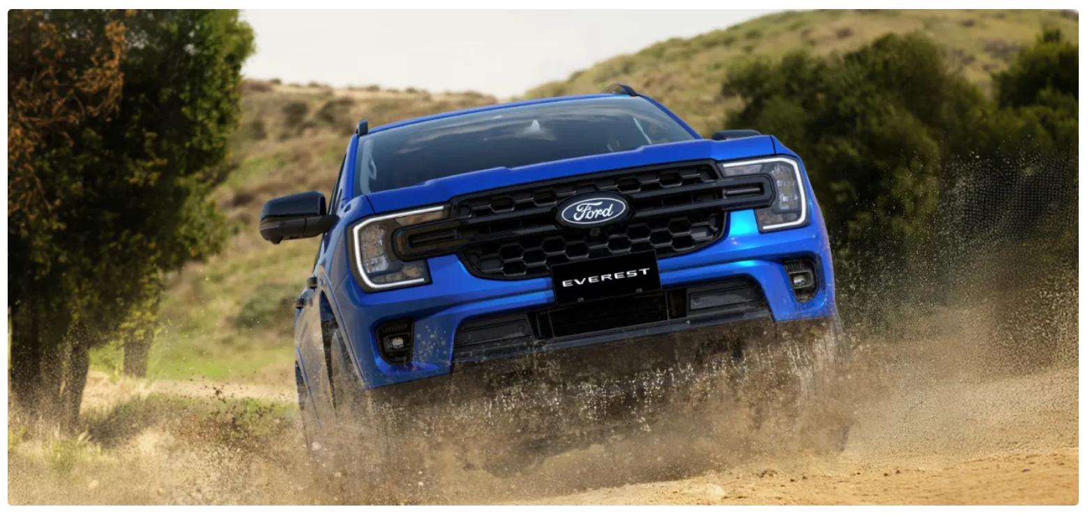 Blue Ford Everest SUV driving through dusty terrain with sparse vegetation and hills in background