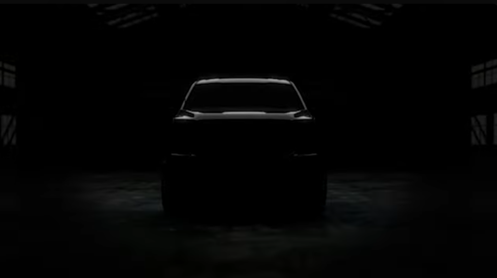 Front view of a dark pickup truck silhouetted in a warehouse setting with overhead lighting highlighting the windshield