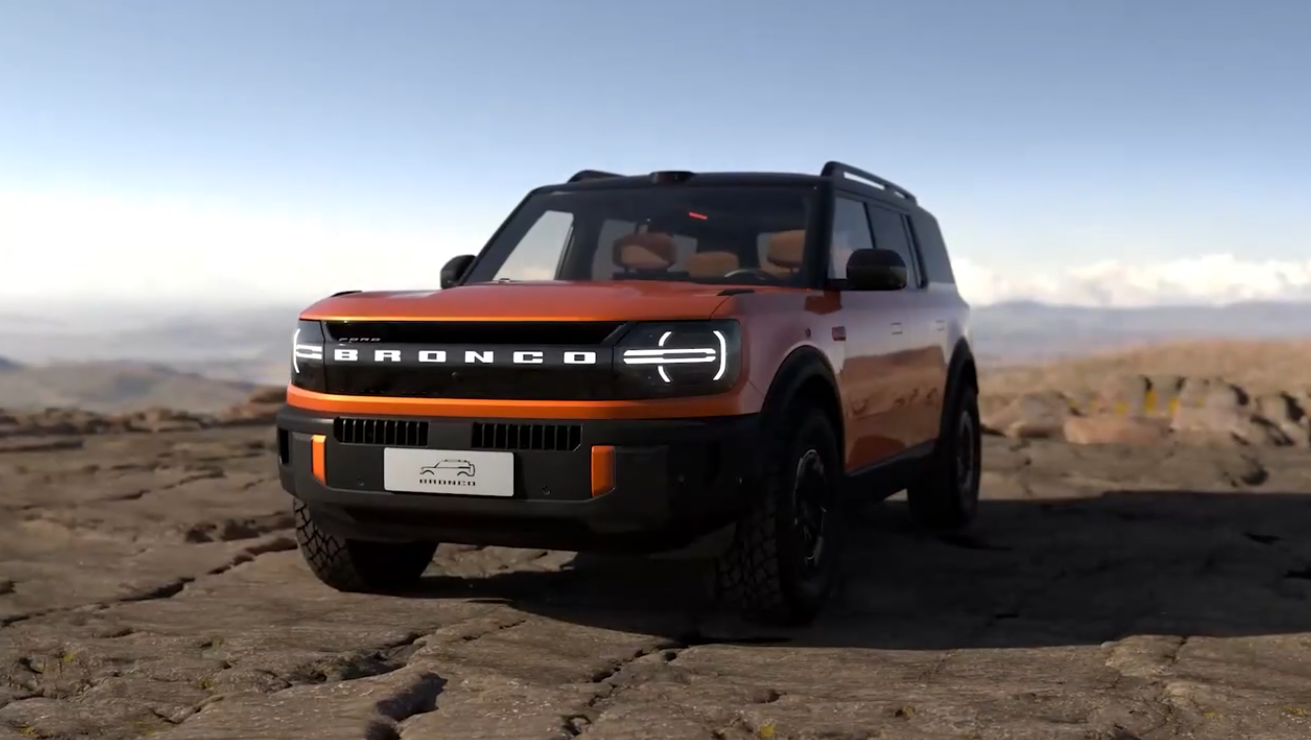 Orange Ford Bronco SUV parked on rocky desert terrain with mountains in background under clear sky