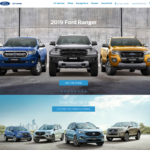 Three 2019 Ford Ranger pickup trucks in blue, black, and gold colors displayed front-facing against a concrete wall backdrop