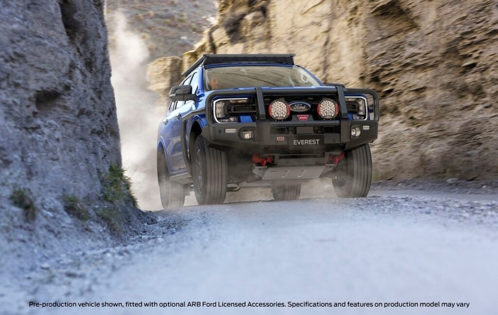 Blue Ford Everest with bull bar and roof rack driving through narrow rocky canyon, kicking up dust