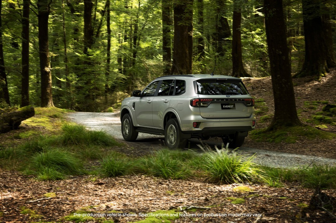 Silver Ford Everest SUV parked on a forest road surrounded by tall trees and undergrowth, rear three-quarter view