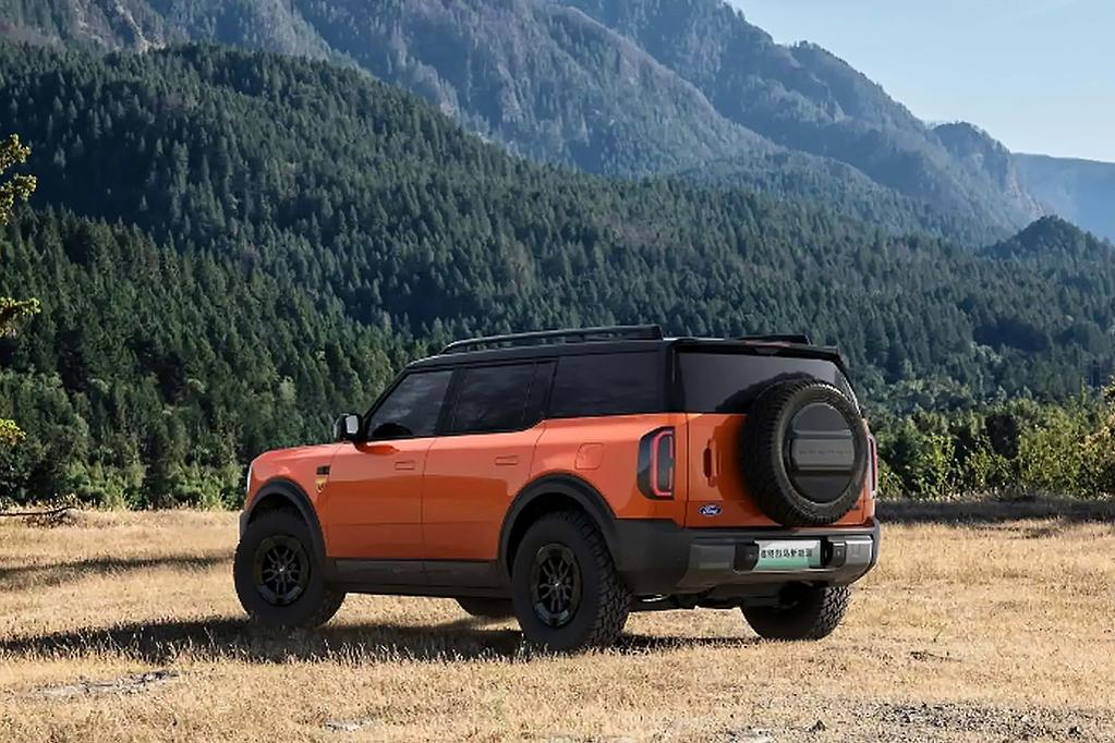 Orange Ford Bronco four-door SUV parked on dirt ground with forested mountains in background