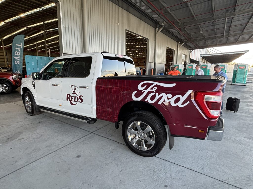 White and maroon Ford F150 pickup truck with Reds team livery parked in an industrial warehouse setting, displaying custom branding on the cab and bed
