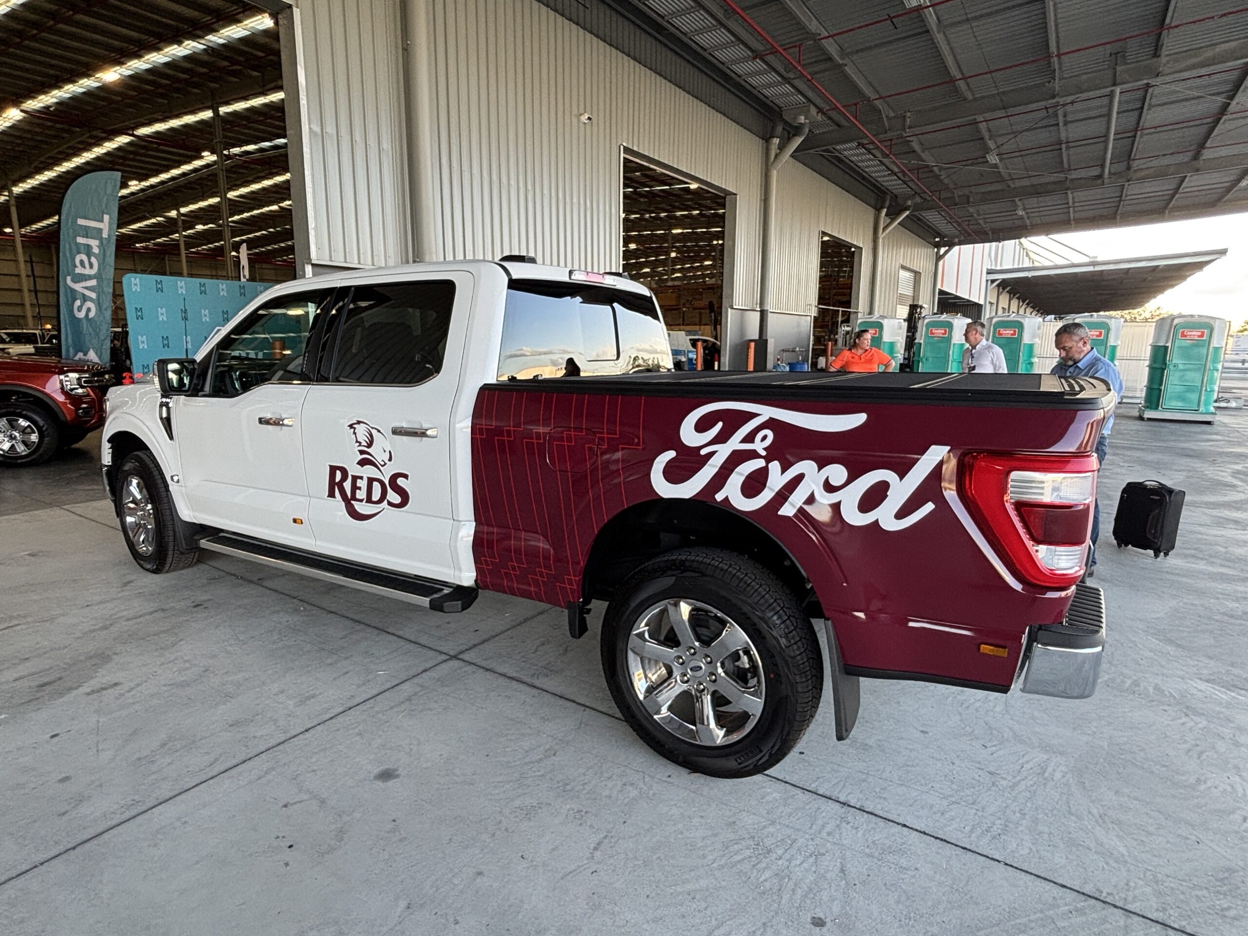 White and maroon Ford F150 pickup truck with Reds team livery parked in an industrial warehouse setting, displaying custom branding on the cab and bed