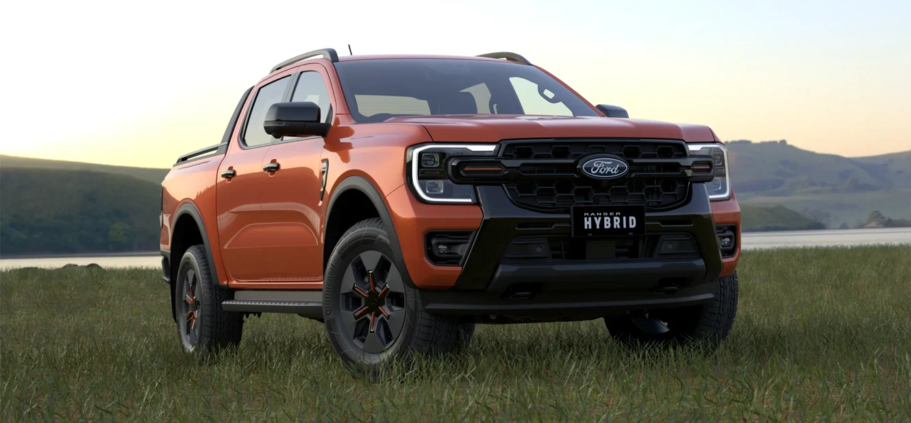 Orange Ford Ranger Hybrid pickup truck parked in grass field with lake and mountains in background at sunset