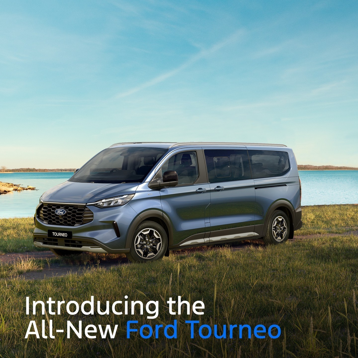 Blue Ford Tourneo minivan parked on grass beside a turquoise lake under clear sky